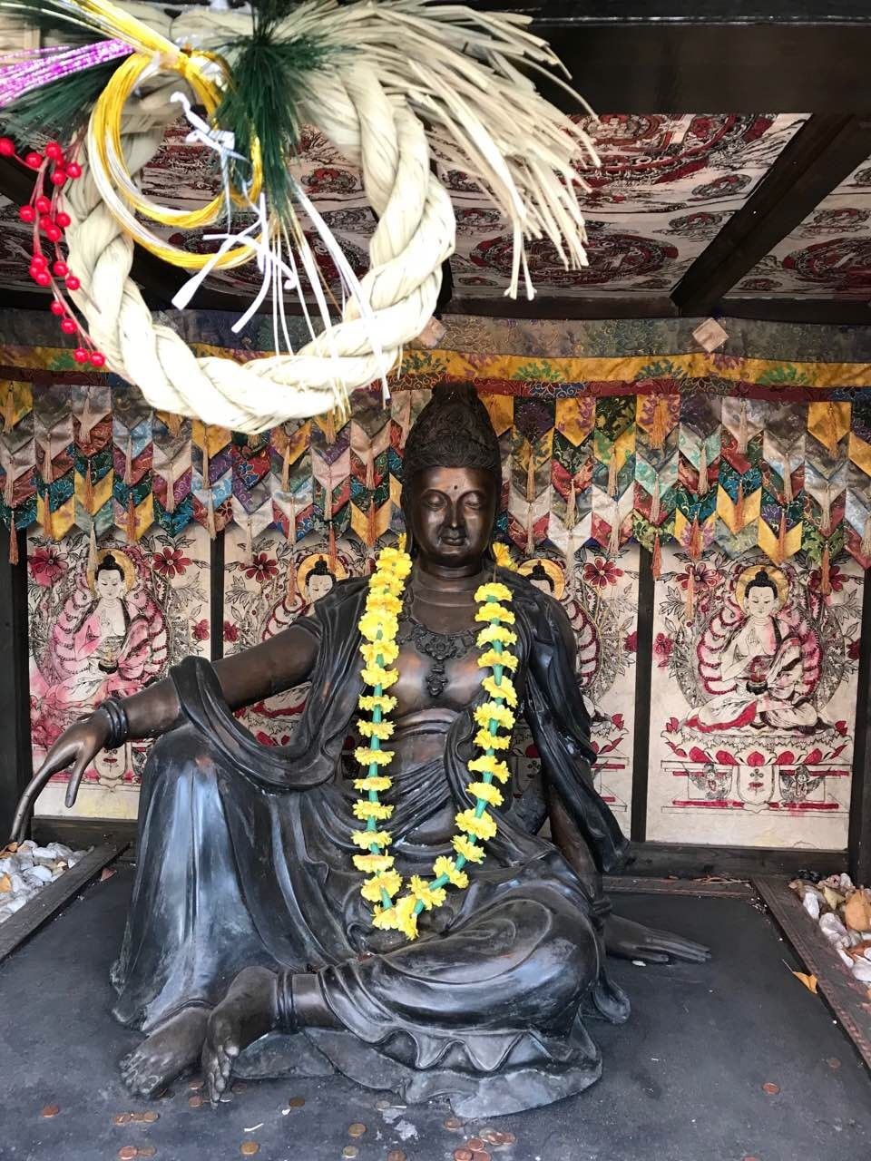 A bronze Buddha with a garland of yellow flowers inside the DOMO museum
